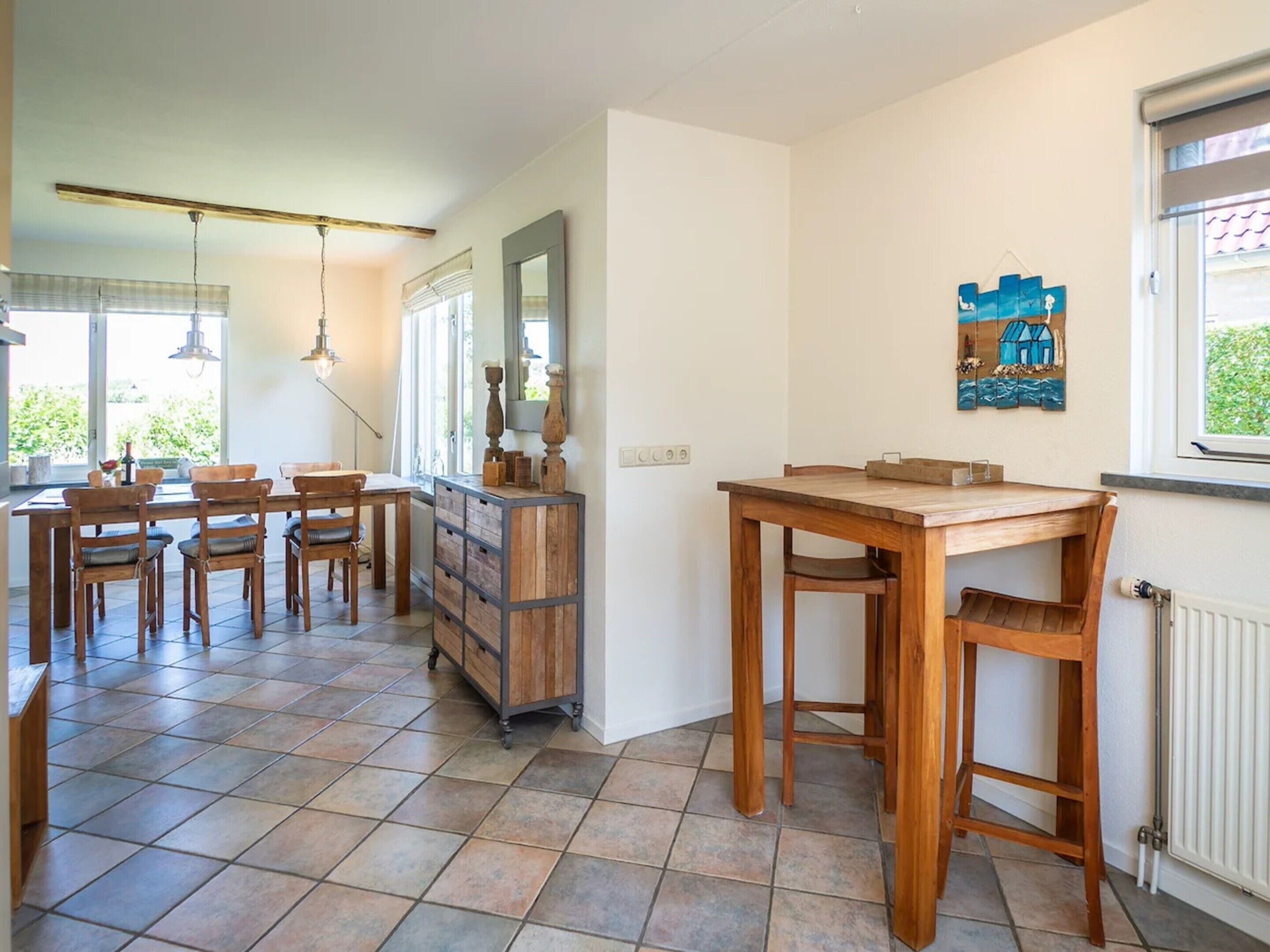 Un coin repas avec une table et des chaises en bois, un meuble avec des tiroirs et une fenêtre donnant sur un paysage verdoyant.