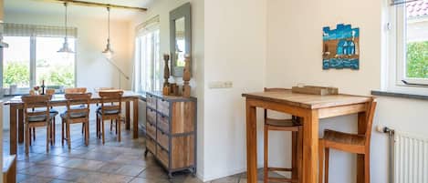 A dining area with a wooden table and chairs, a cabinet with drawers, and a window with a view of greenery.