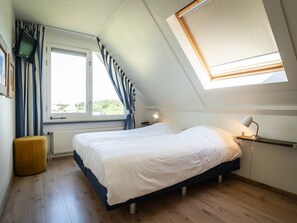 A bedroom with a bed, a window with curtains, a bedside table with a lamp, and a skylight. - Texel Getaway With Whirlpool (De Koog)