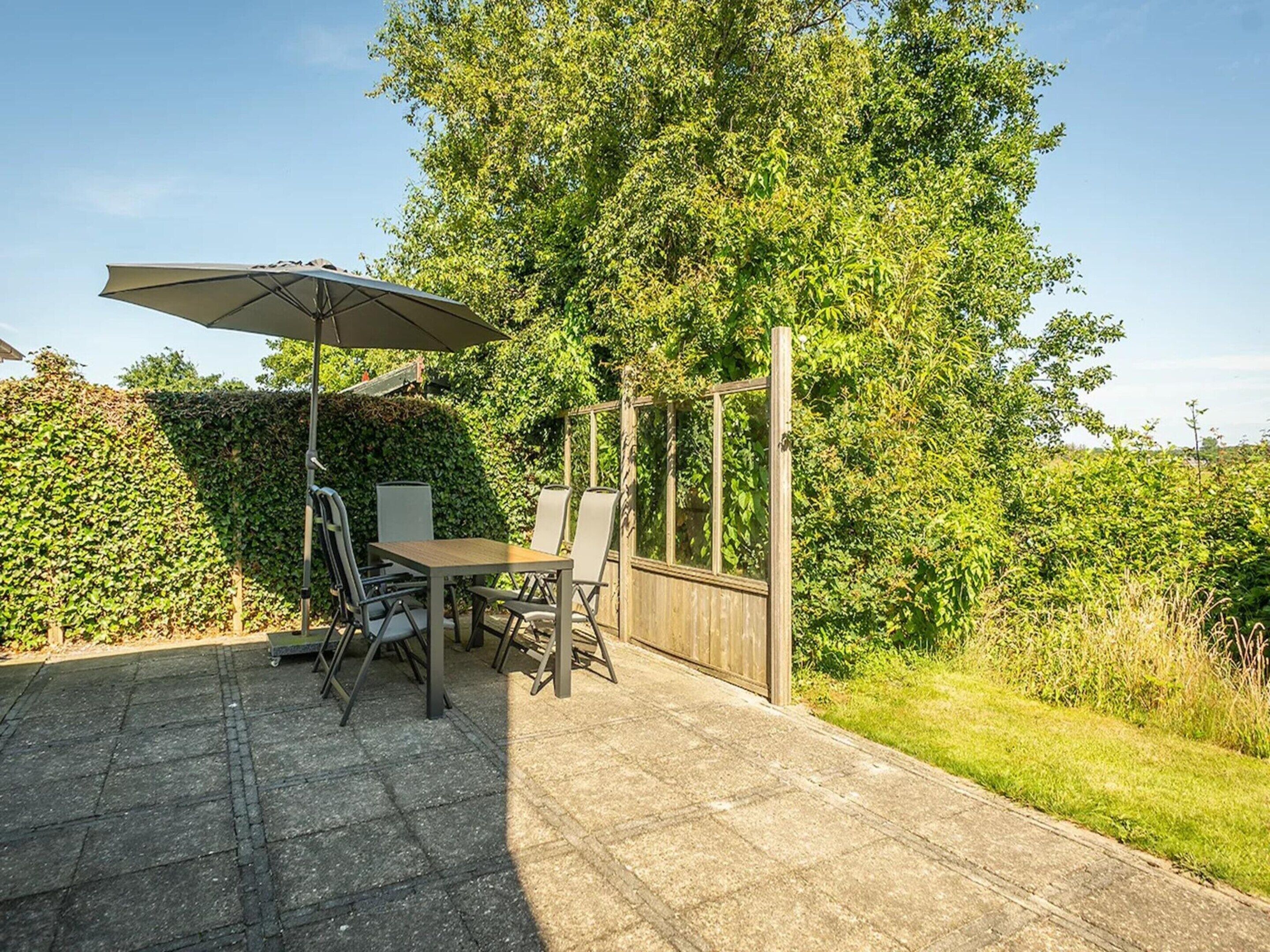 Un patio al aire libre con mesa y sillas, una pérgola de madera y un paraguas grande.