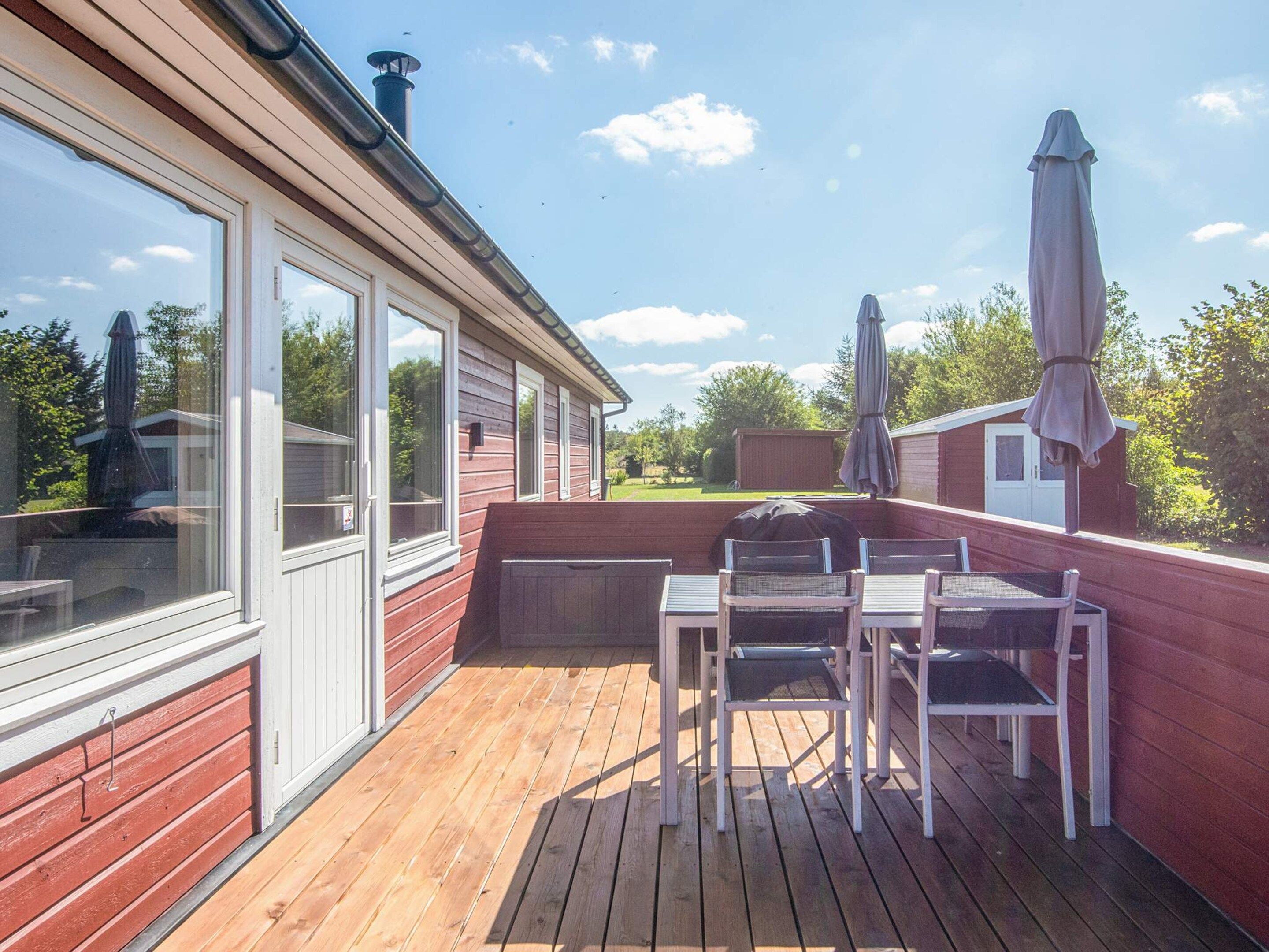 Une terrasse en bois avec une table et des chaises, un barbecue abrité et une vue sur la maison voisine.