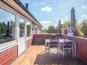 A wooden deck with a table and chairs, a covered grill, and a view of a neighboring house. - 8 Person Holiday Home in Hovborg (Hovborg)