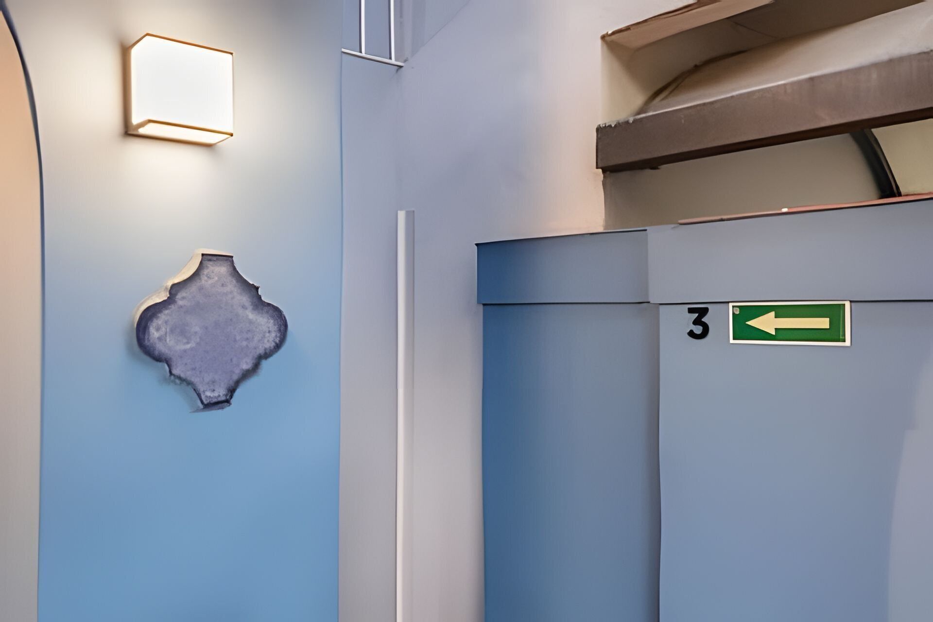 A hallway with a blue wall, a decorative piece, a door with a number sign, and an arrow sign.