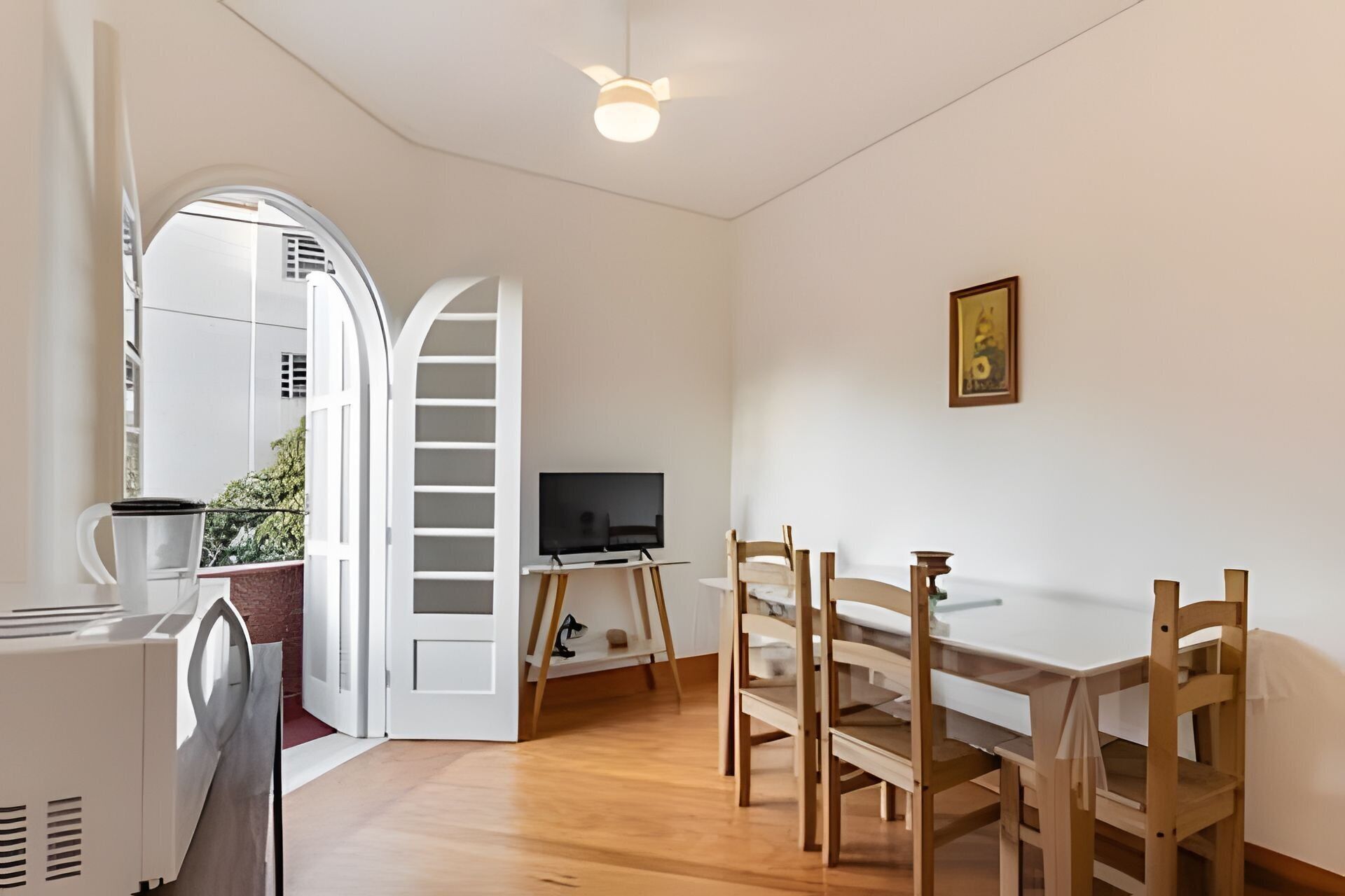 Une pièce comprenant une table à manger, des chaises, un téléviseur et une porte blanche donnant sur un espace extérieur.
