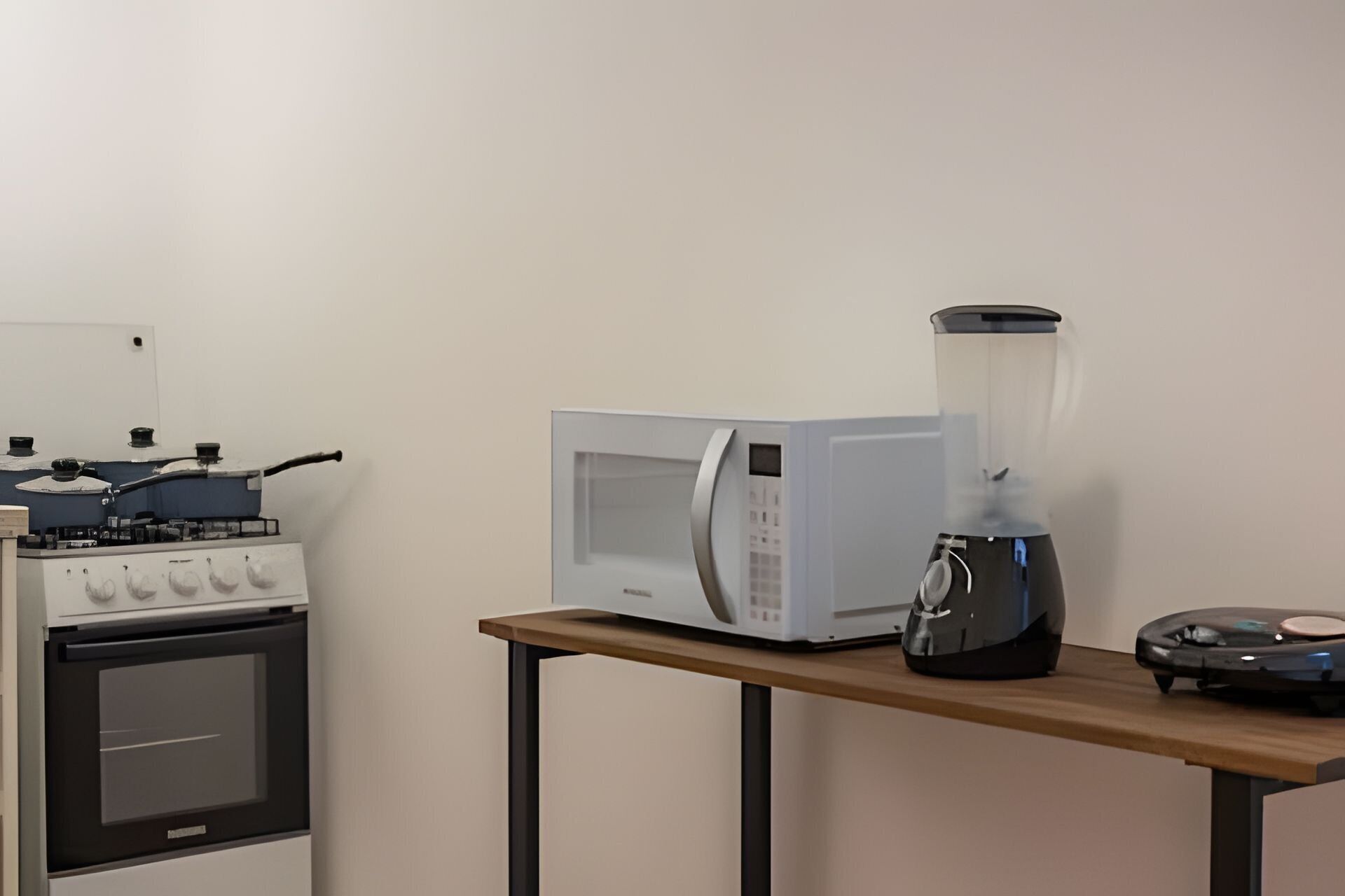 A kitchen with a stove, microwave, and blender on a wooden table.