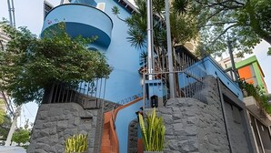 A modern building with a curved blue facade, a staircase leading to an upper level, and stone walls. - Aconchego Cotoxó - Loft 3 (São Paulo)