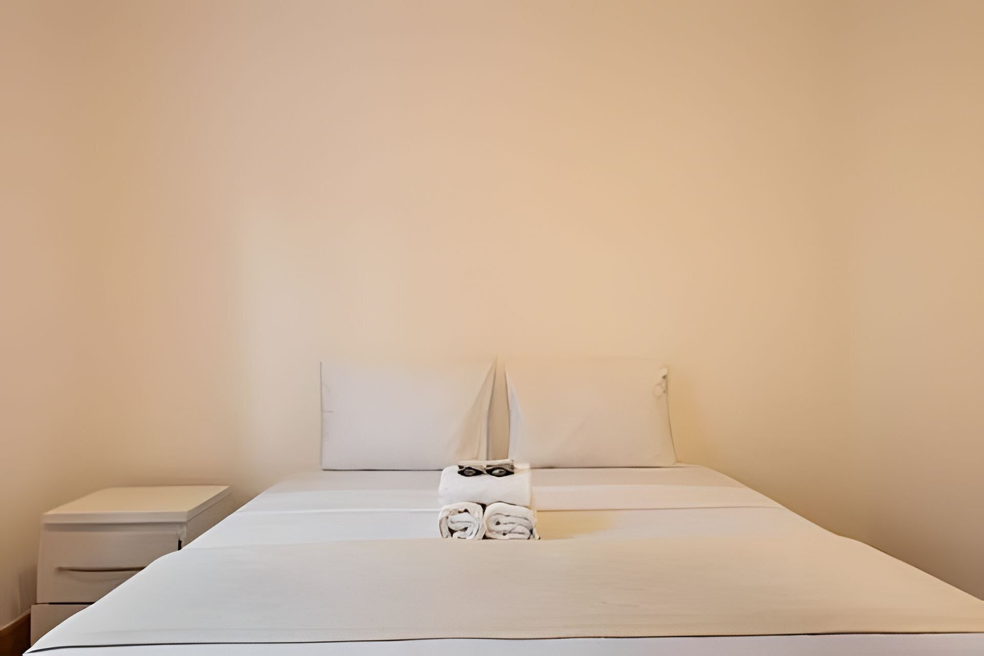 A single bed with a white mattress, a pillow, and a folded towel on the bed.