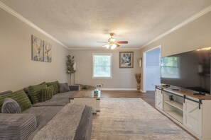 A living room with a sectional sofa, a flat-screen TV, and a ceiling fan.