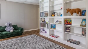 Una stanza con un divano verde, una libreria bianca e un tappeto decorato.