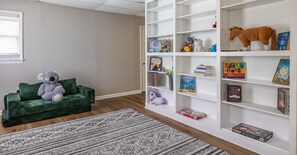 A room with a green sofa, a white bookshelf, and a patterned rug. - Mins to Truist Park & The Battery | Spacious East Cobb Home for Groups (Marietta)