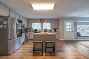 A modern kitchen with a central island, stainless steel appliances, and a view to the outside. - Mins to Truist Park & The Battery | Spacious East Cobb Home for Groups (Marietta)