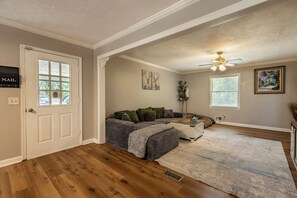 A living room with a sectional sofa, a ceiling fan, and a large window. - Mins to Truist Park & The Battery | Spacious East Cobb Home for Groups (Marietta)