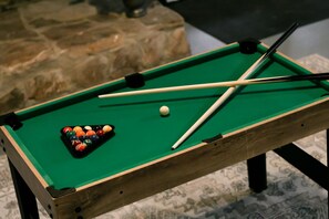 Een pooltafel met een groene viltbekleding, een set poolkeus en een rek met biljartballen.