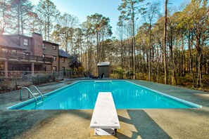 Una piscina rectangular con plataforma de hormigón, rodeada de árboles y un edificio de fachada de ladrillo.
