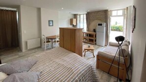 Een slaapkamer met een bed, nachtkastje, lamp en uitzicht op een keukenhoek.