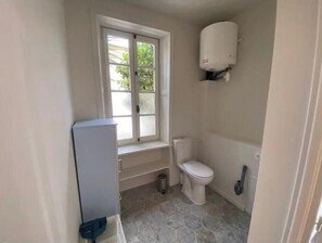 A bathroom with a toilet, a window, and a water heater. - Charming studio apartment with a pool (Courçon)