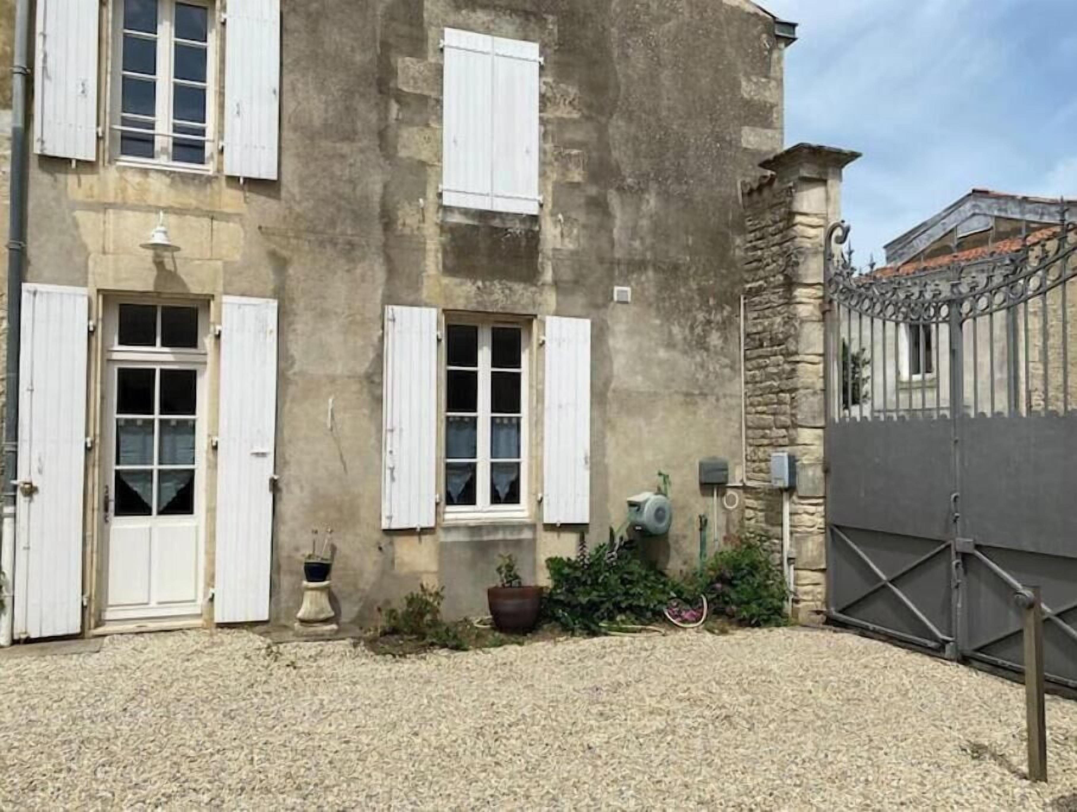 Un bâtiment avec des volets blancs, un mur en pierre et un portail en métal.