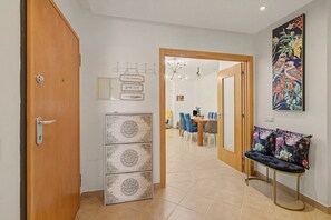 A hallway with a wooden door, a wall-mounted light fixture, a decorative cabinet, and a dining area with a table and chairs. - Apartment 'Magnolia' with Private Terrace, Wi-Fi and Air Conditioning (Tavira)