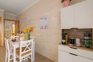 A modern kitchen with a coffee machine, a dining table with chairs, and decorative wall art. - Apartment 'Magnolia' with Private Terrace, Wi-Fi and Air Conditioning (Tavira)