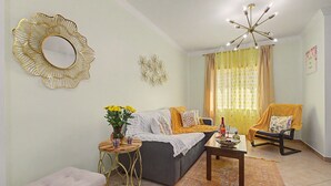 Uma sala de estar com sofá, mesa de centro, mesa lateral, espelho decorativo, lustre e tapete estampado.