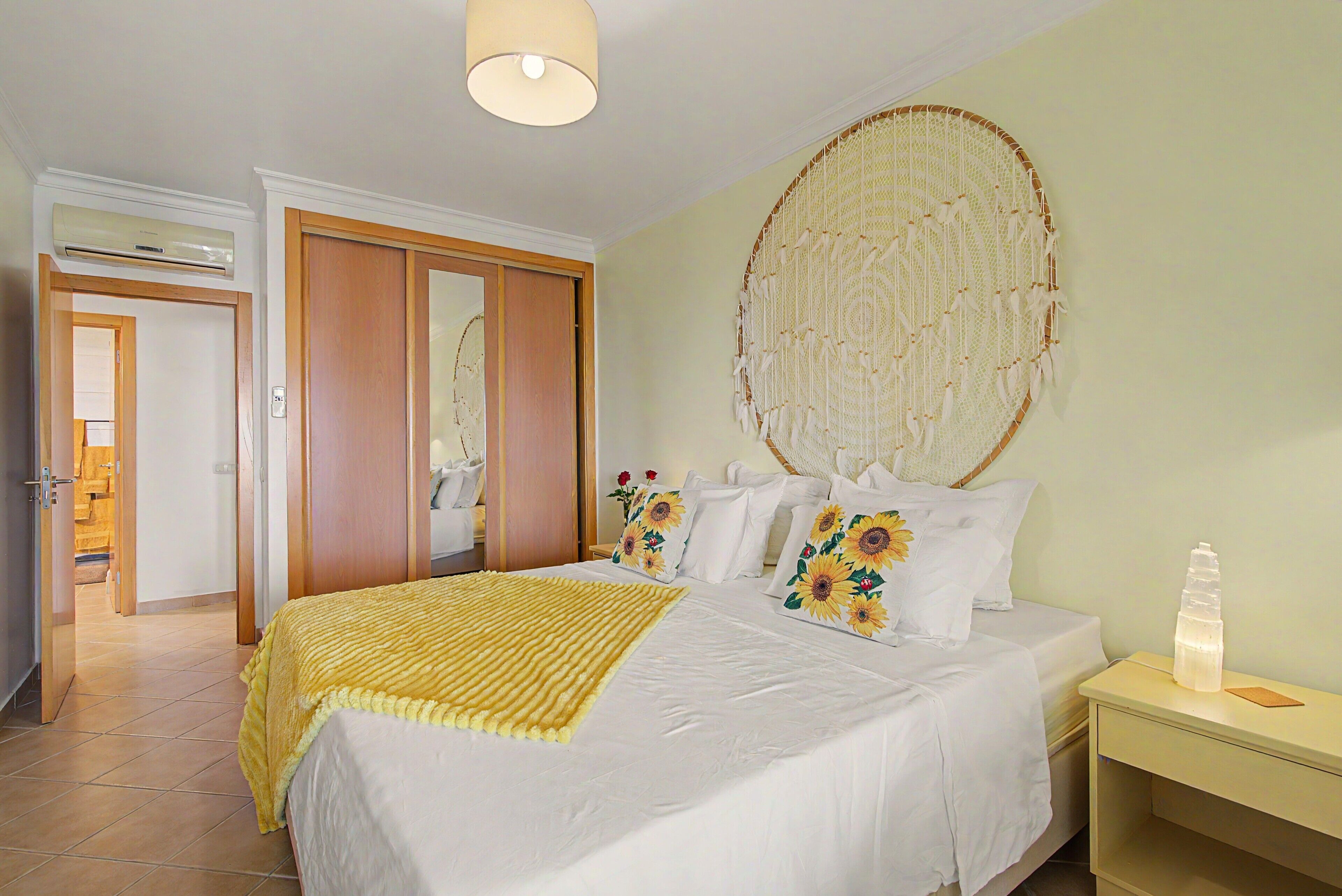 Un dormitorio con cama, almohadas, una mesita de noche, un cuadro en la pared y una puerta.