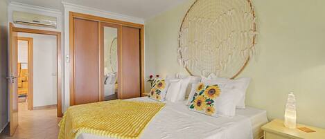 A bedroom with a bed, pillows, a bedside table, a wall hanging, and a door.