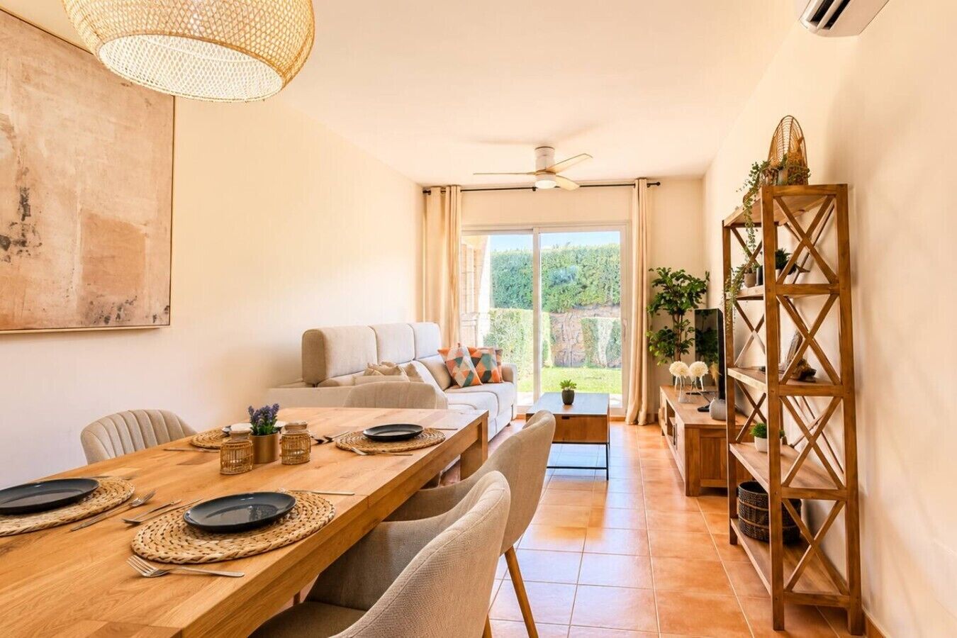 Un coin repas avec une table en bois dressée pour deux personnes, un canapé et une vue sur l’extérieur.