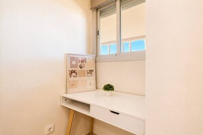 Ein weißer Schreibtisch mit Korkwand, einer kleinen Pflanze und einem Fenster mit Jalousien.