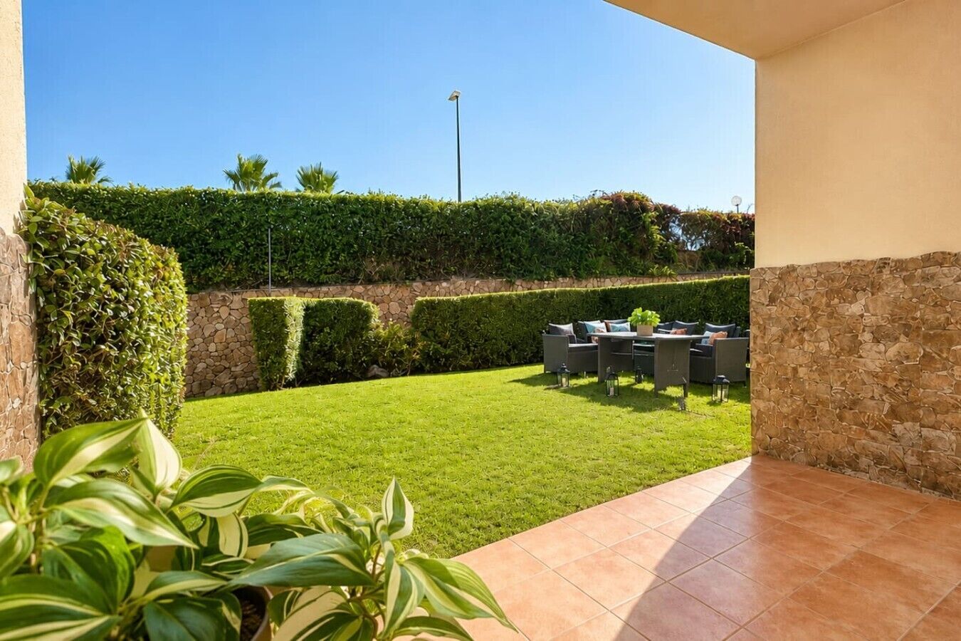 A patio area with a lawn, a stone wall, and outdoor furniture.