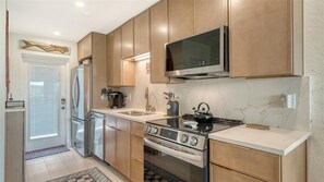 A modern kitchen with stainless steel appliances, wooden cabinets, and a large microwave. - Jamaica Royale 032 by Tropical Sands Accommodations (Siesta Key)