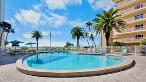 Ein Swimmingpool mit Liegestühlen, Palmen und einem Gebäude mit Balkonen.