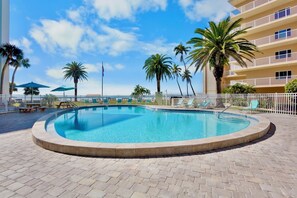 Ein Swimmingpool mit Liegestühlen, Palmen und einem Gebäude mit Balkonen.