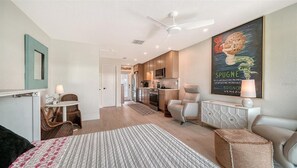 Un salon moderne comprenant un canapé, une table à manger avec des chaises, un coin cuisine avec des placards et des appareils électroménagers, et un ventilateur de plafond.