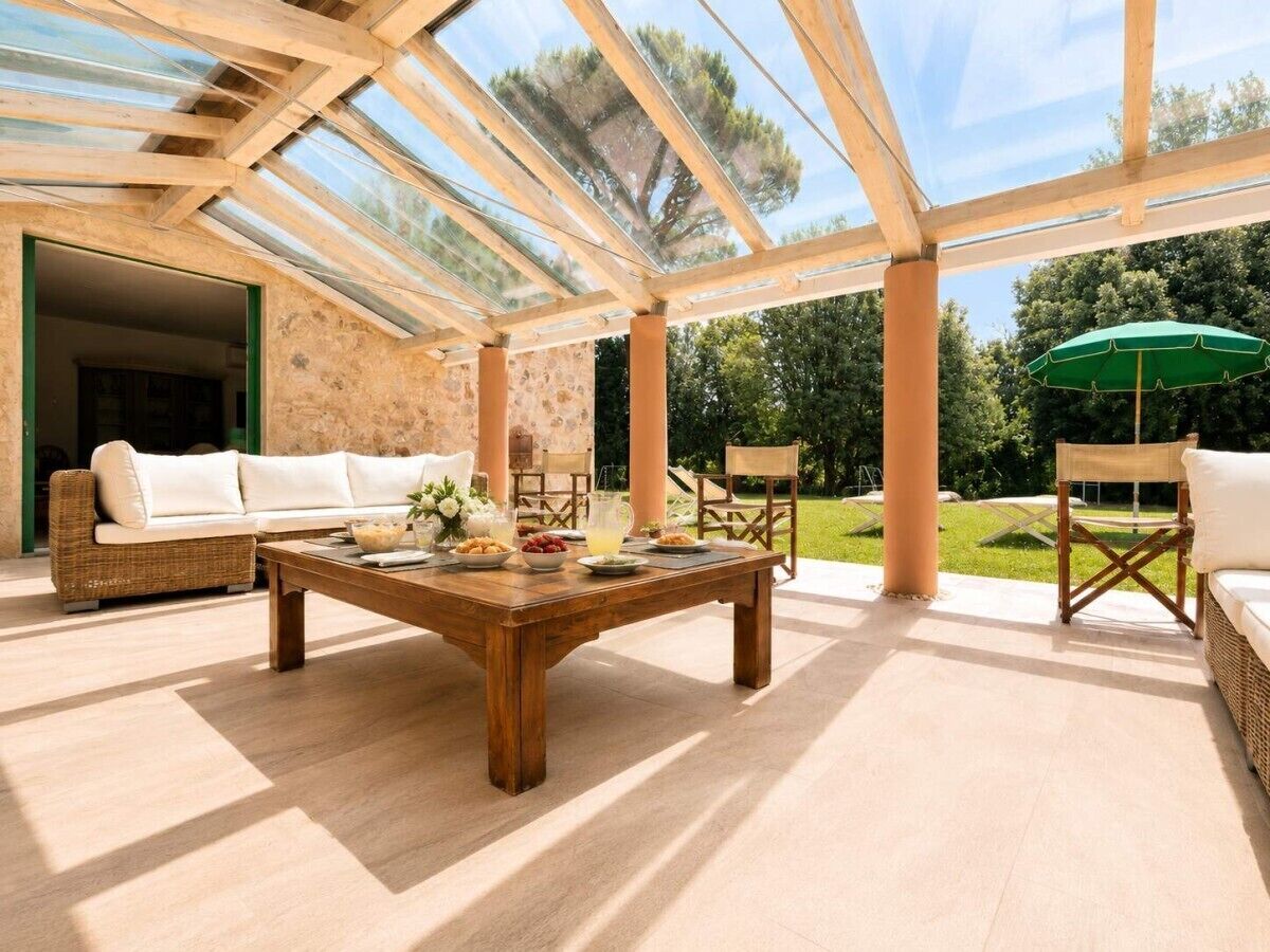 A spacious patio with a wooden table, wicker furniture, and a glass ceiling.