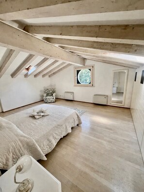 Ein Schlafzimmer mit schrägen Wänden, einem Bett, einem Sessel, einem kleinen Fenster und einem Spiegel.