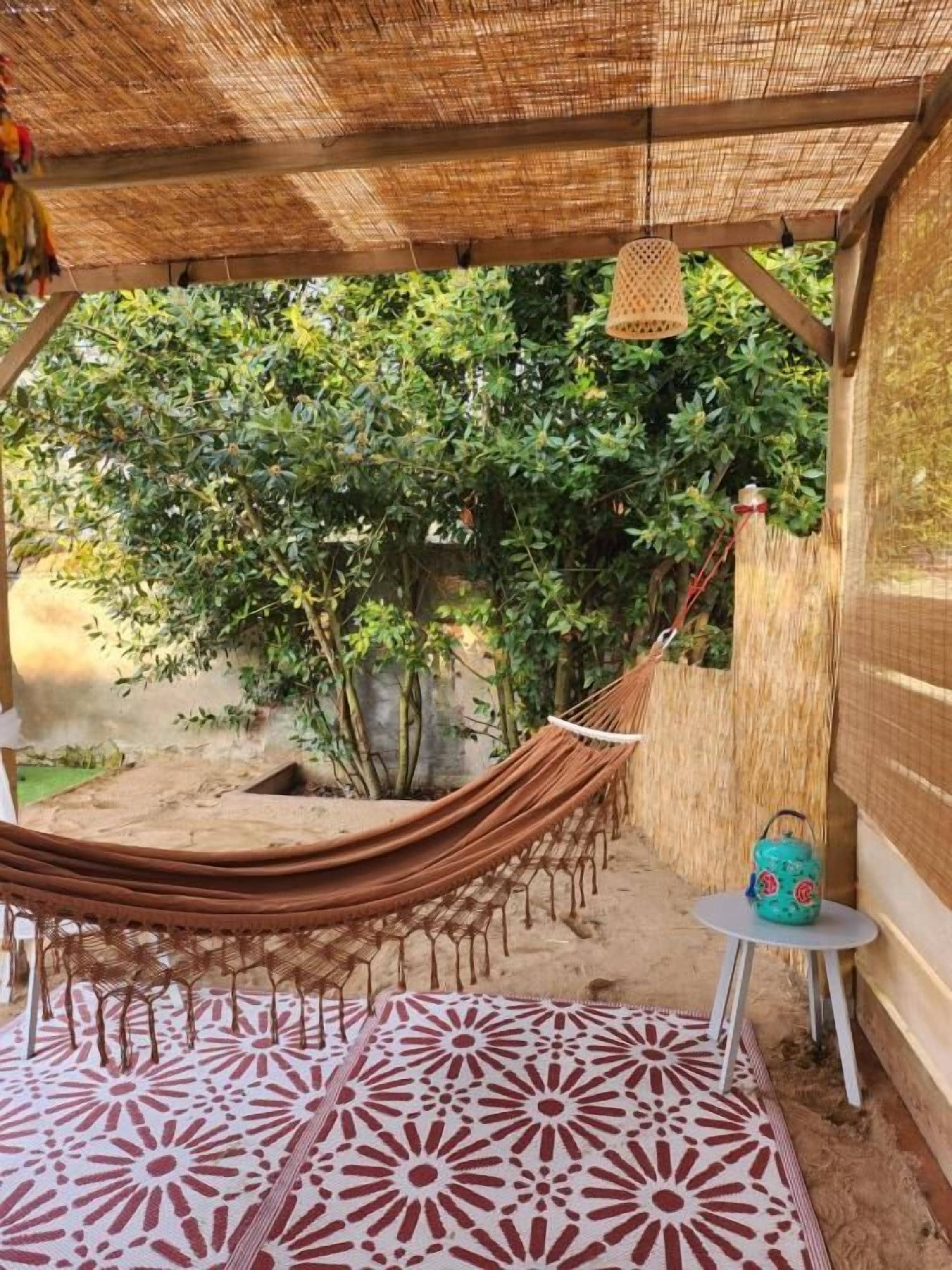 A hammock under a thatched roof, a patterned floor, and a small table with a decorative item.