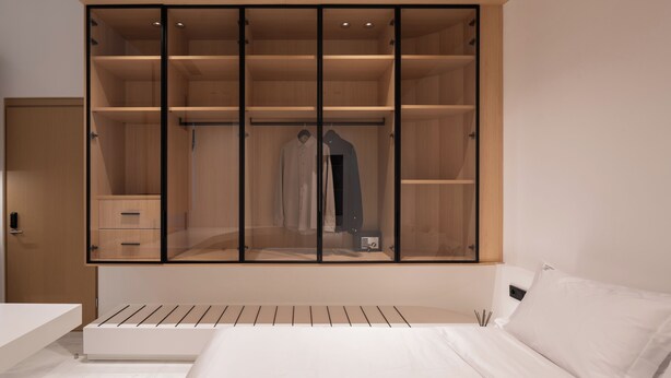 A bedroom with a bed, a wardrobe with multiple shelves, and a bedside table. - The George Athens (Athens)