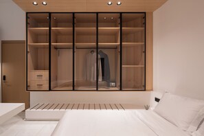 A bedroom with a bed, a wardrobe with multiple shelves, and a bedside table. - The George Athens (Athens)