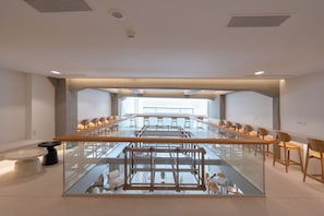 Een ruime vergaderzaal met een lange tafel, stoelen en een glazen balustrade met uitzicht op een lager gelegen niveau.
