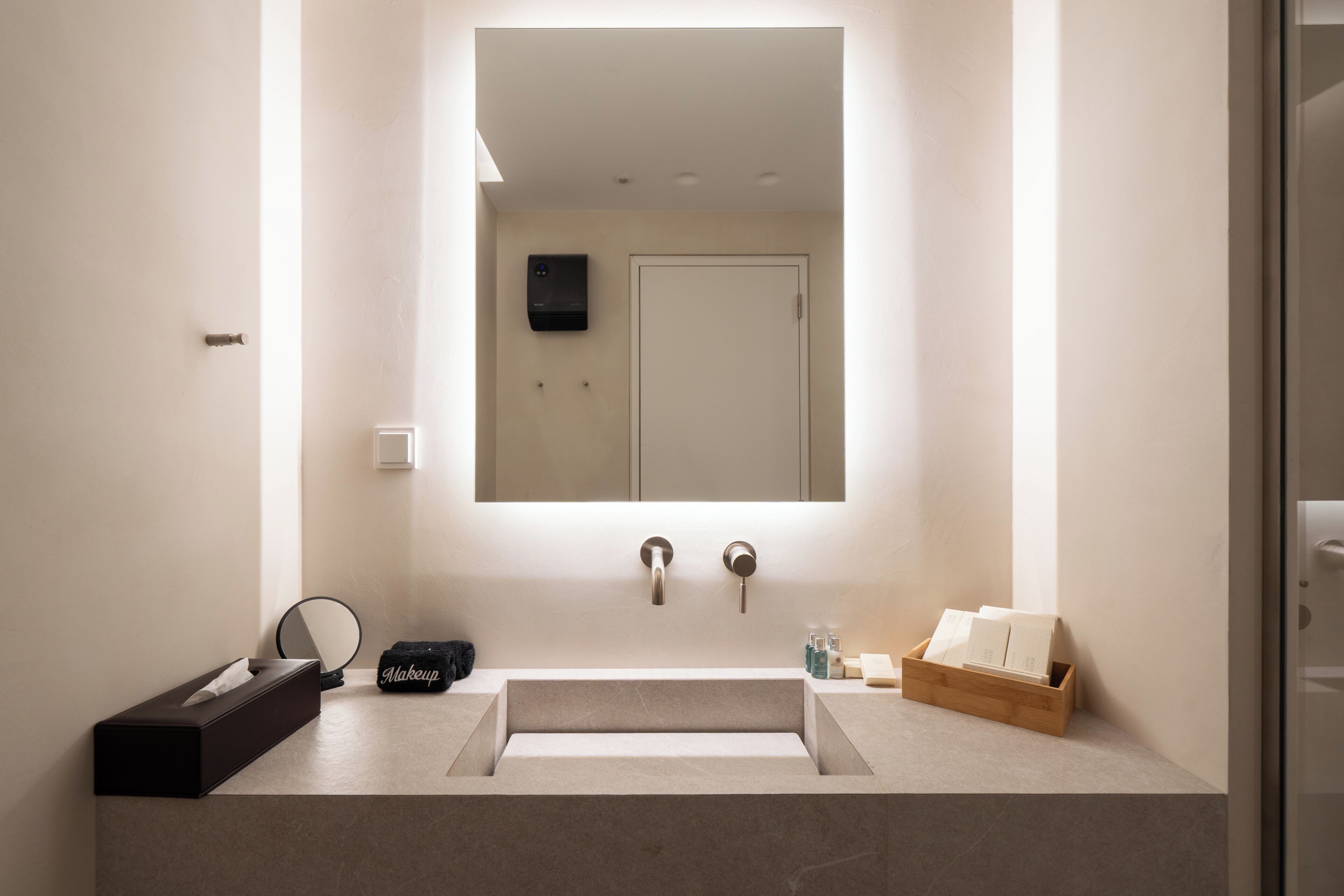 A modern bathroom with a large mirror, two sinks, and a vanity area with toiletries.