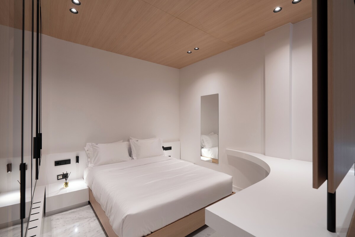 Un dormitorio moderno con una cama grande, una mesita de noche, un espejo y televisión integrada.