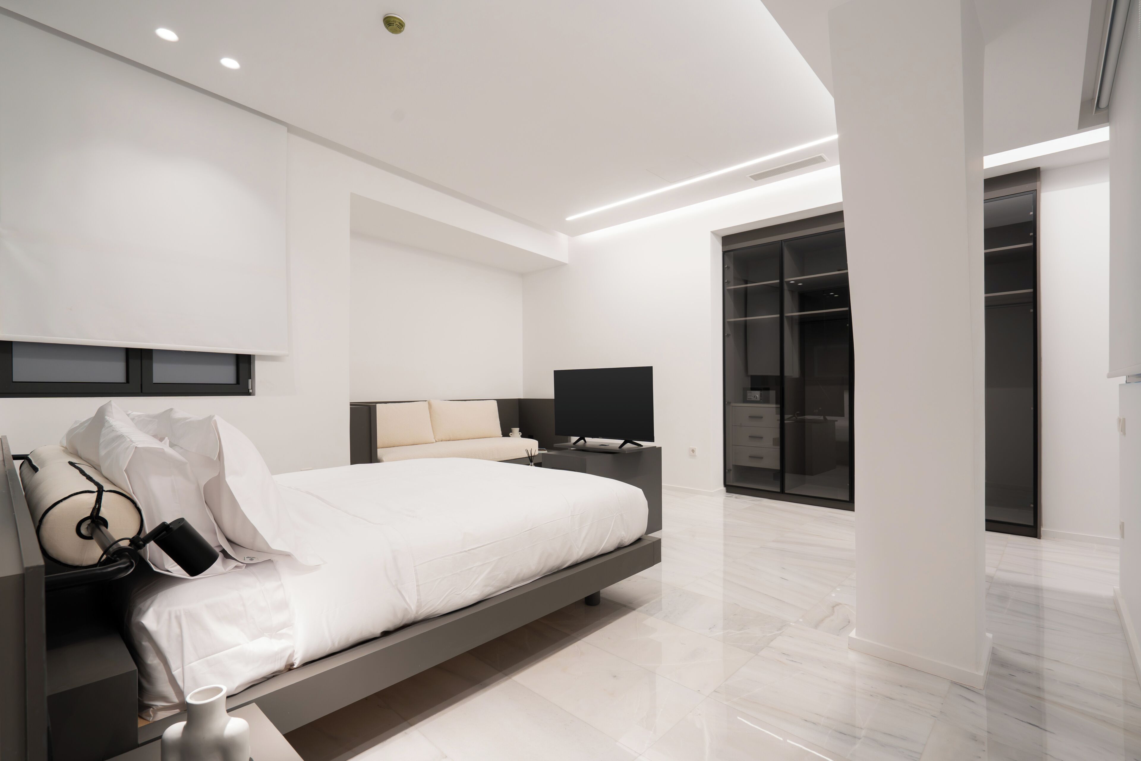 A modern bedroom with a large bed, bedside tables, a TV, and a walk-in closet.