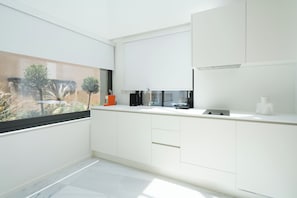 Een moderne keuken met witte kasten, een zwarte koffiezetapparaat en uitzicht op een tuin door een raam.