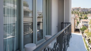 A balcony with a metal railing, a window with a view of a cityscape, and a white pedestal. - The George Athens (Athens)