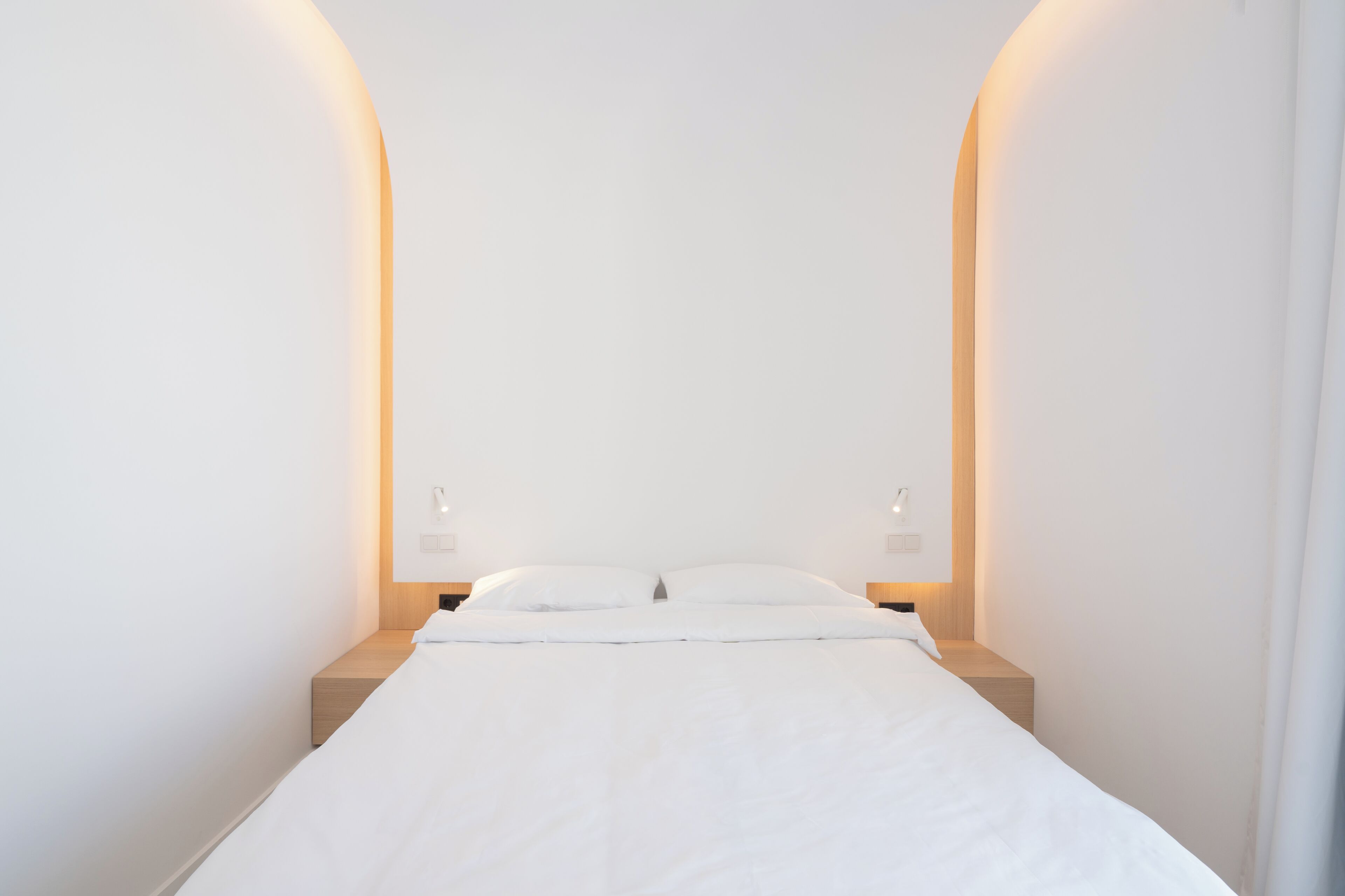 Habitación de hotel minimalista con una cama individual, dos mesitas de noche e iluminación en la pared.