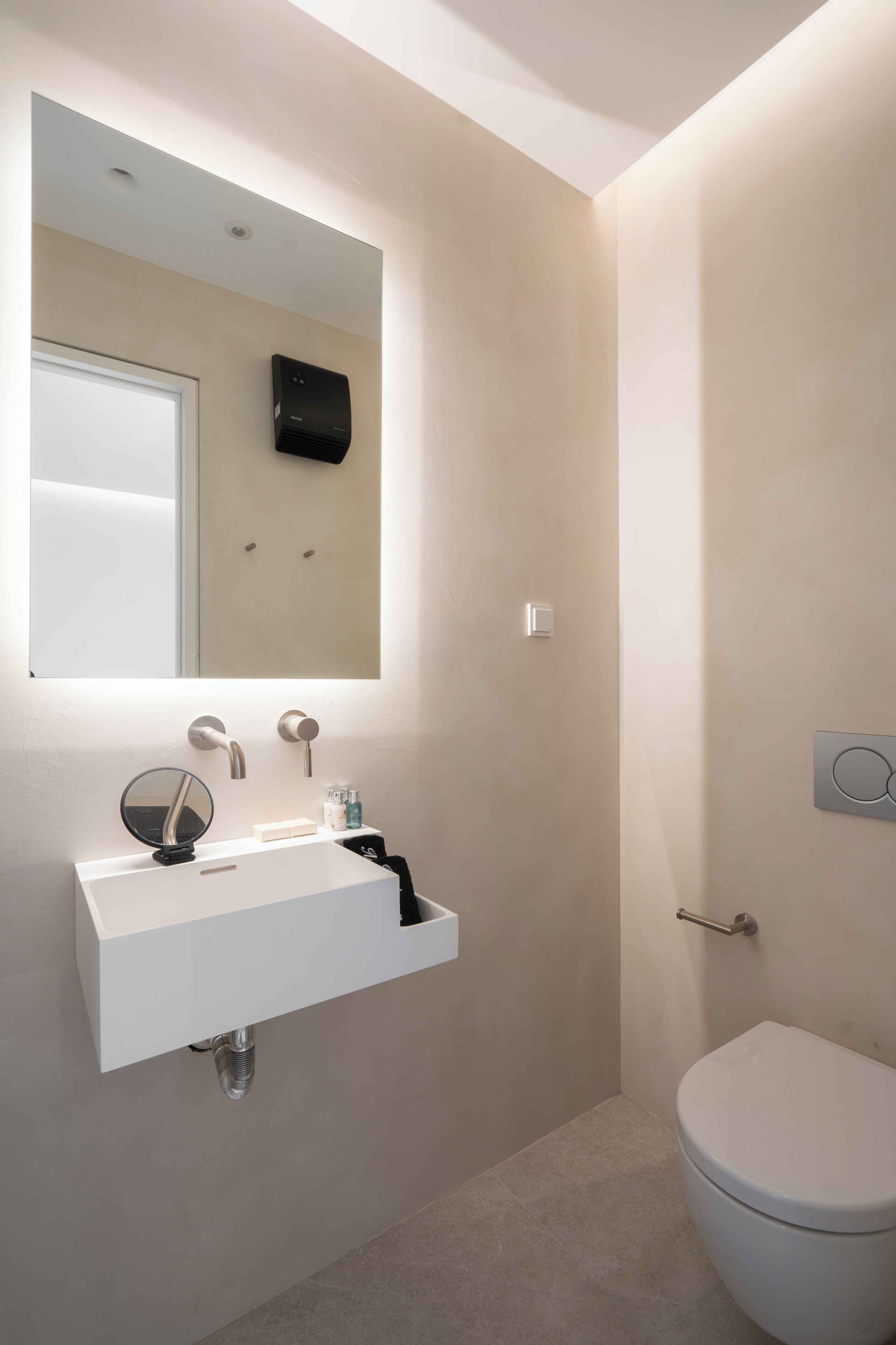 Un baño moderno con un lavamanos blanco, un espejo, un inodoro y un perchero para toallas.