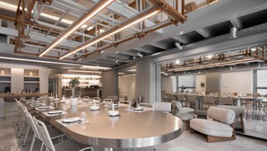 A modern dining area with a large round table, white chairs, and a bar area with shelves of bottles. - The George Athens (Athens)