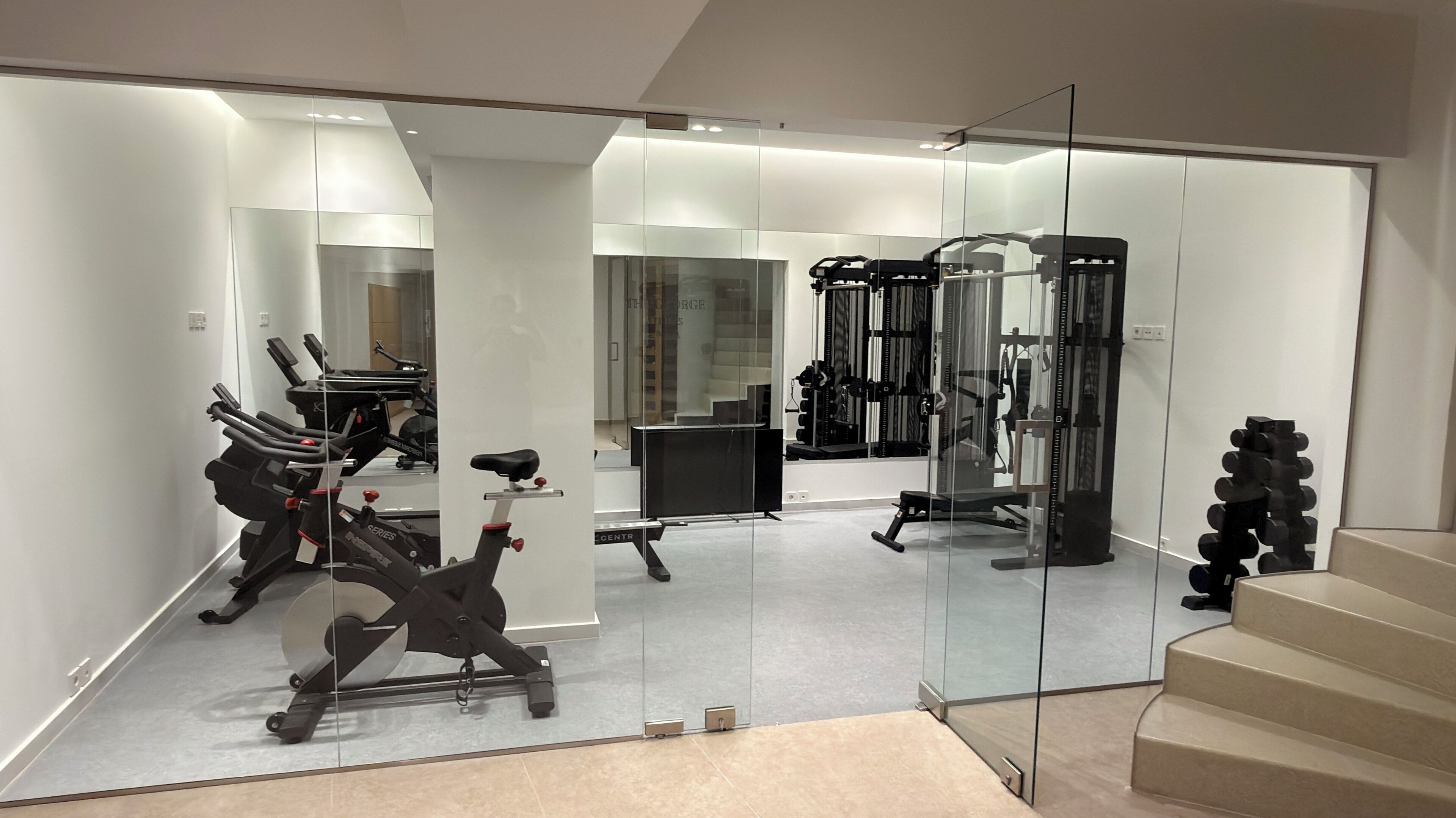 A modern gym with exercise equipment, a weight bench, and a staircase.