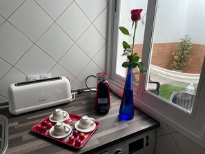 Une cuisine équipée d’un grille-pain, d’une bouilloire, d’un plateau avec des théières, d’une rose dans un vase et d’une fenêtre donnant sur un jardin.