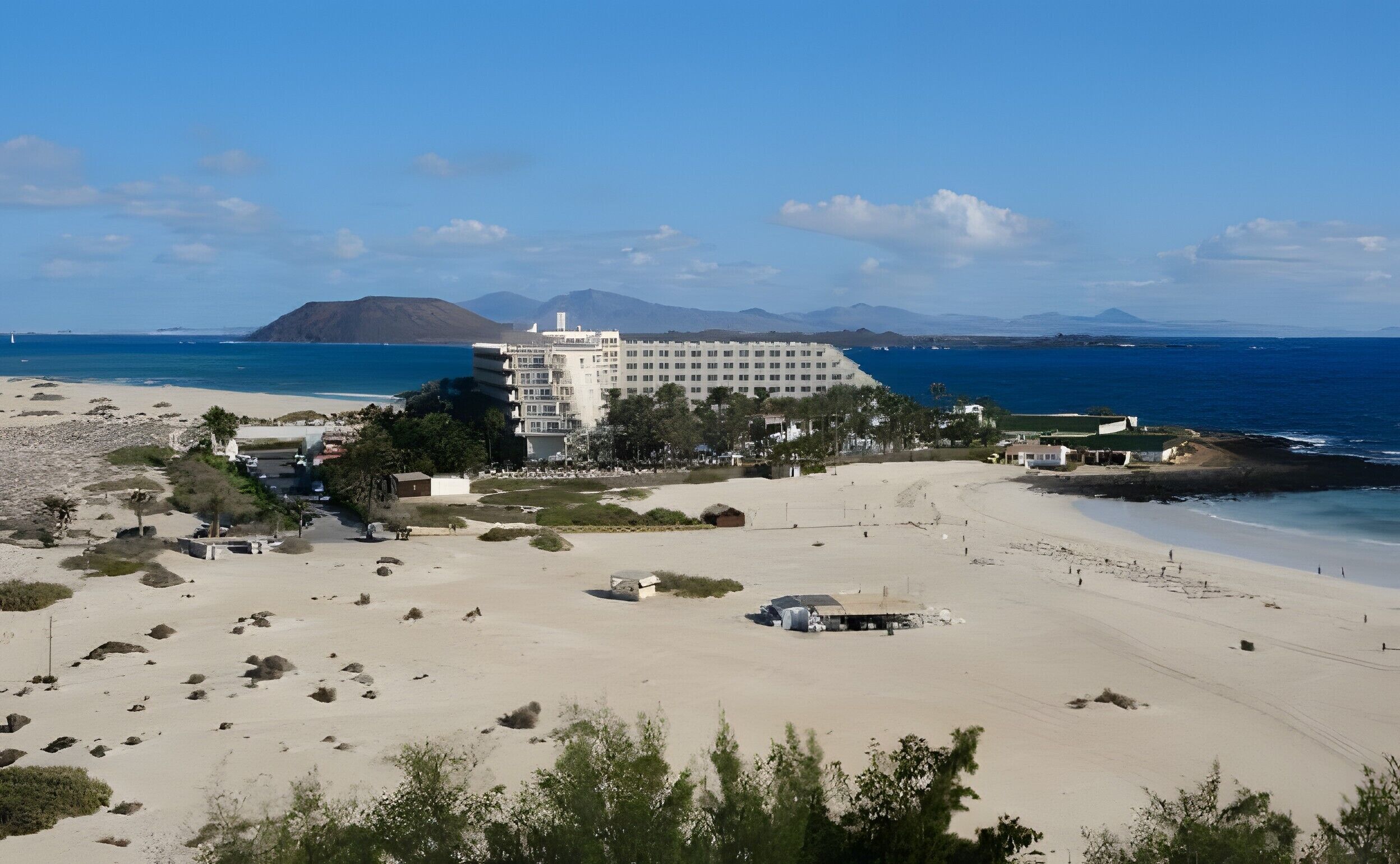 Een kusthotel met uitzicht op het strand, meerdere gebouwen en een bergachtige achtergrond.